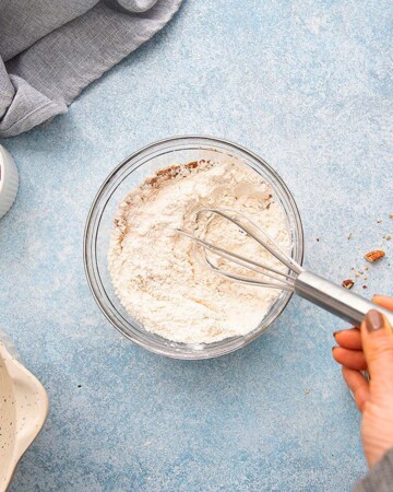 a hand whisking white flour in a small glass bowl. 