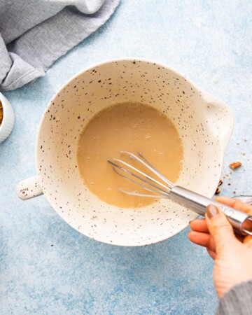 a hand whisking brown batter in a white bowl.