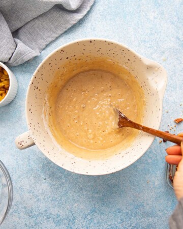 a hand mixing orange cake batter in a white bowl using a brown wooden spoon.