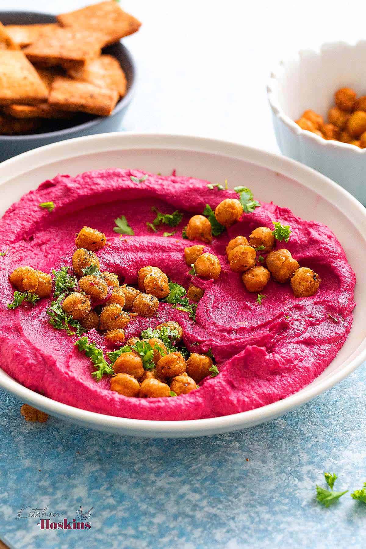 white bowl with pink hummus and garnished with chickpeas and parsley. 