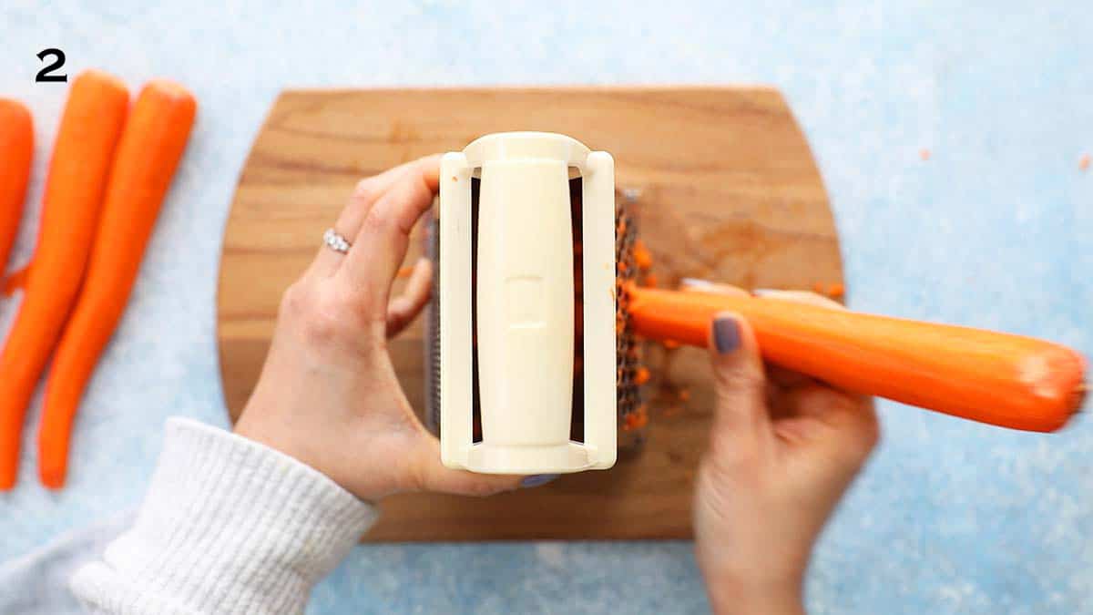 two hands grating one carrot using a box grater.