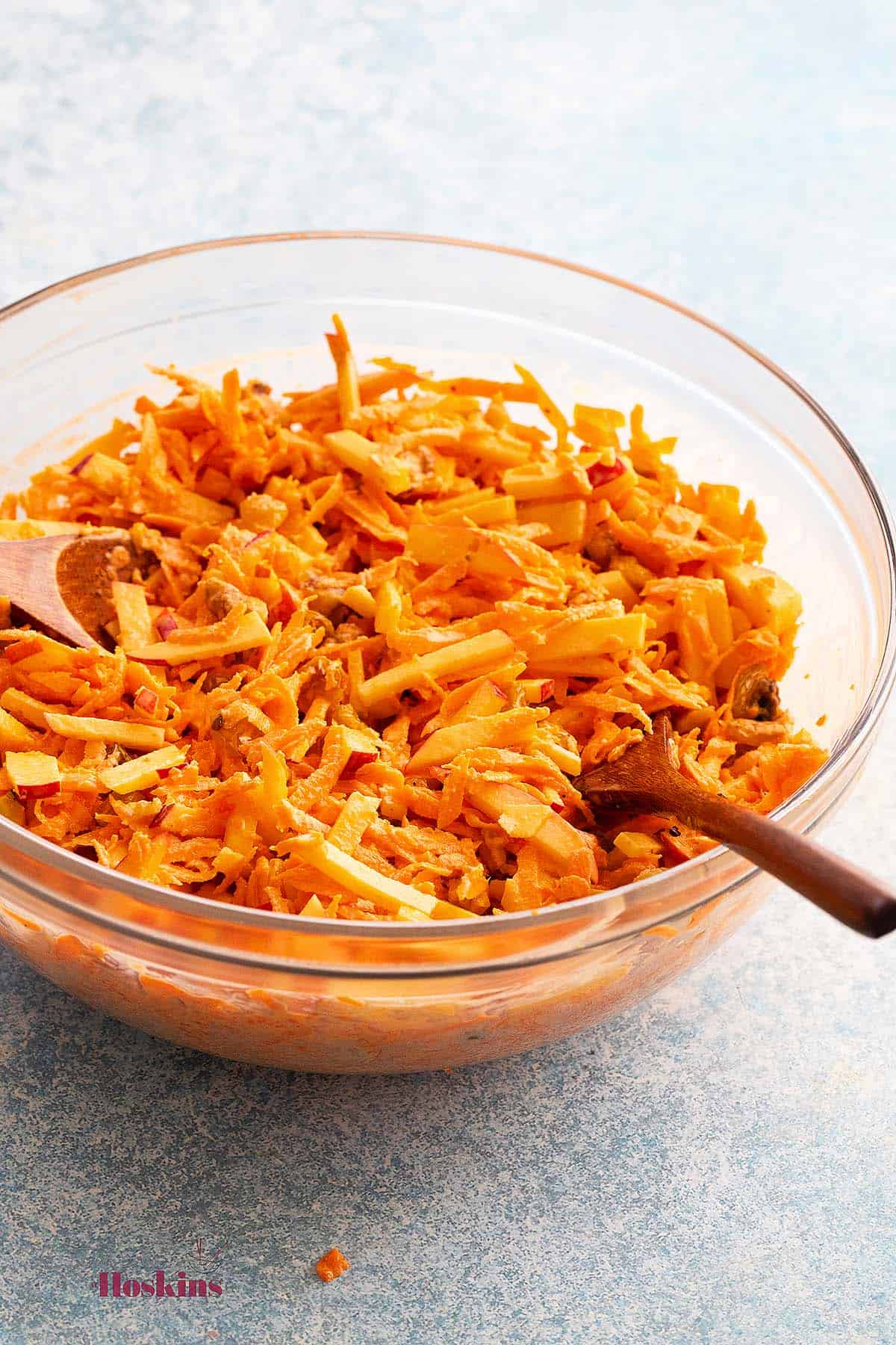 one large glass bowl with prepared carrot salad and two brown wooden spoons. 