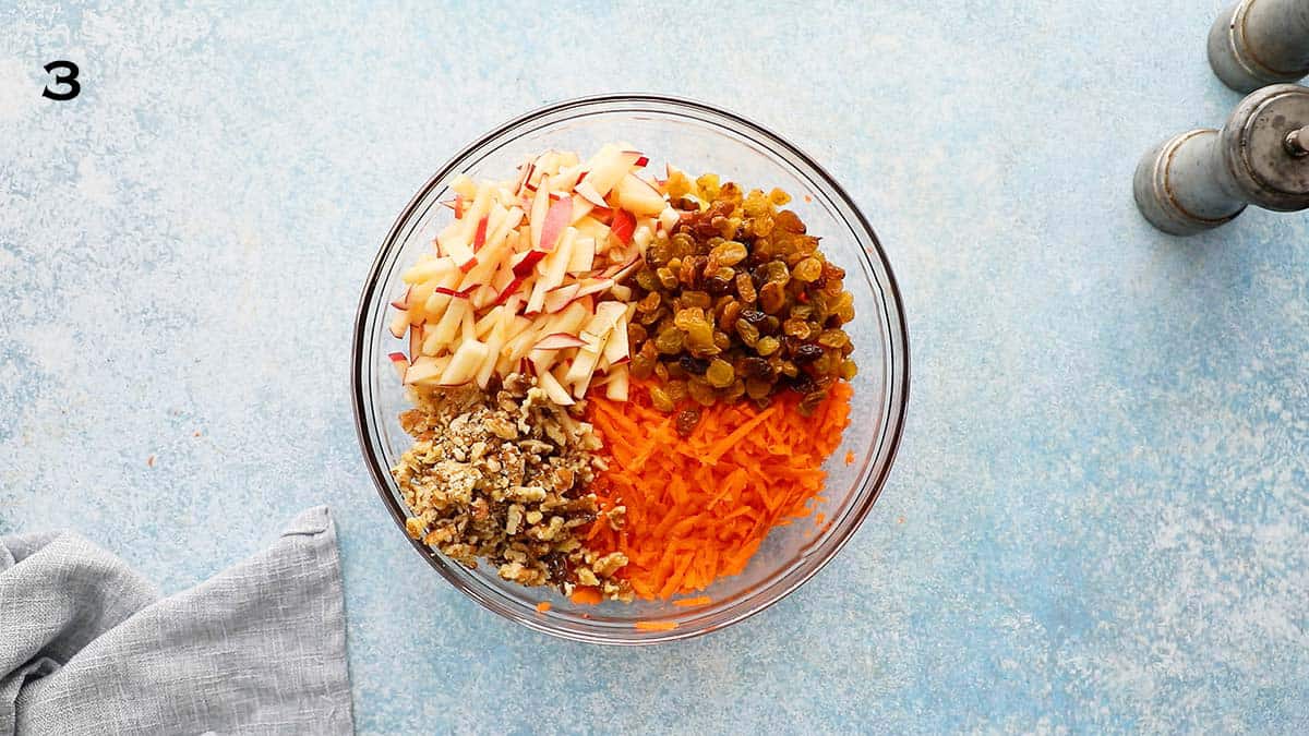 one large glass bowl with grated carrots, raisins, chopped apples and walnuts,