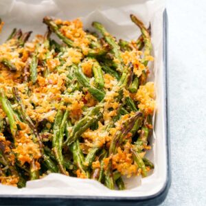 cooked green beans topped with golden crumbs in a white tray.