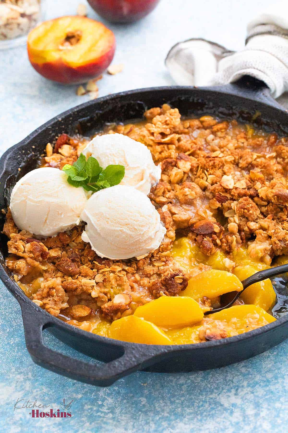 black skillet with baked peach crumble and topped with 3 scoops of vanilla ice cream.