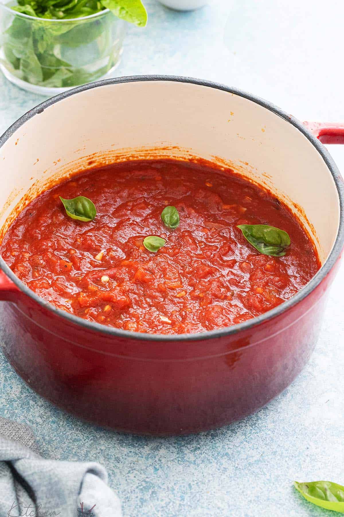 white pan with red handles, filled with red sauce and garnished with basil leaves.