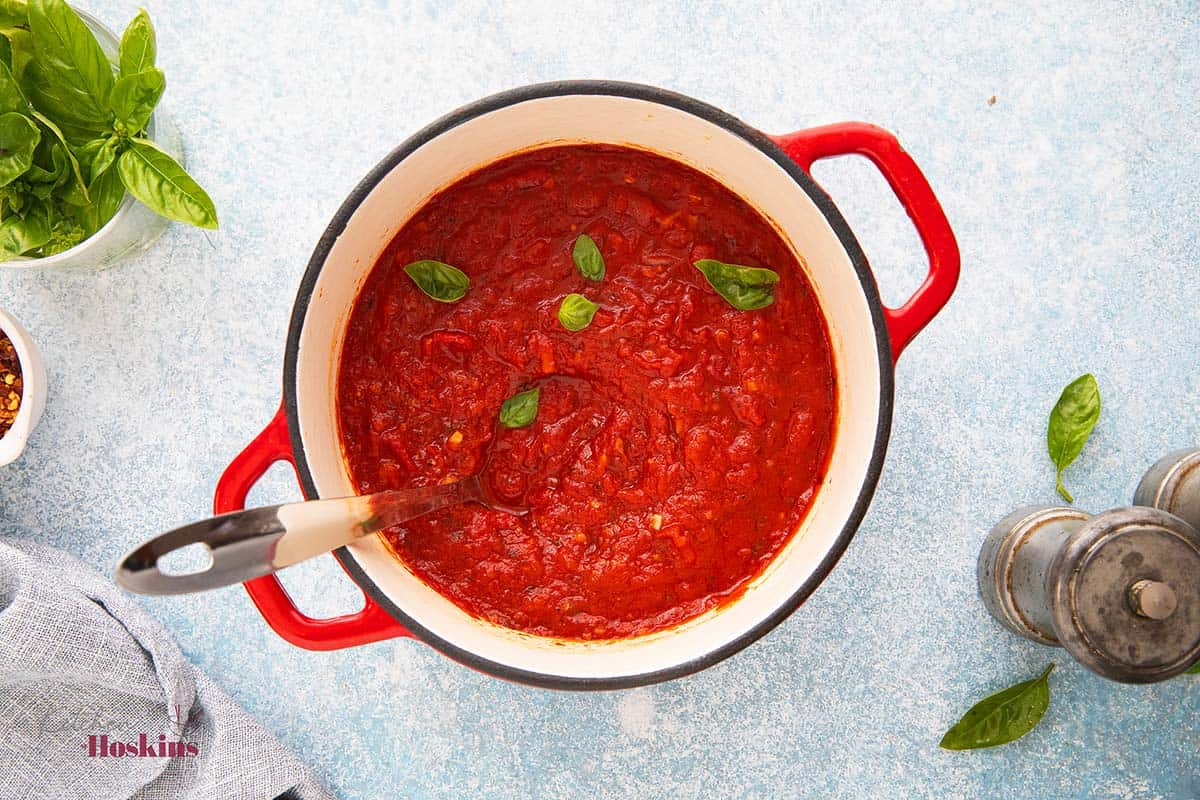 white pan with red handles, filled with red sauce and garnished with basil leaves.