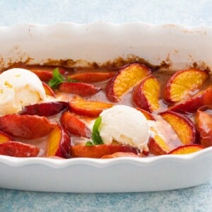 baked peach wedges in a white fluted baking dish, along with 2 scoops of vanilla ice cream.