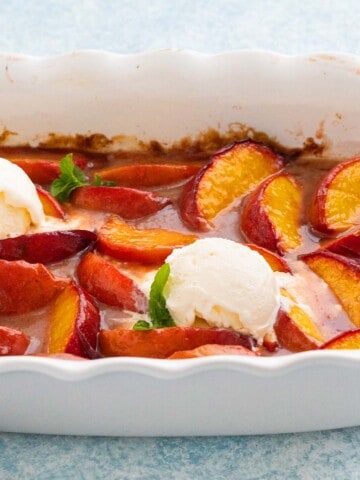 baked peach wedges in a white fluted baking dish, along with 2 scoops of vanilla ice cream.
