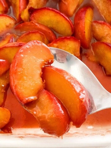 yellow baked peaches in a white dish.
