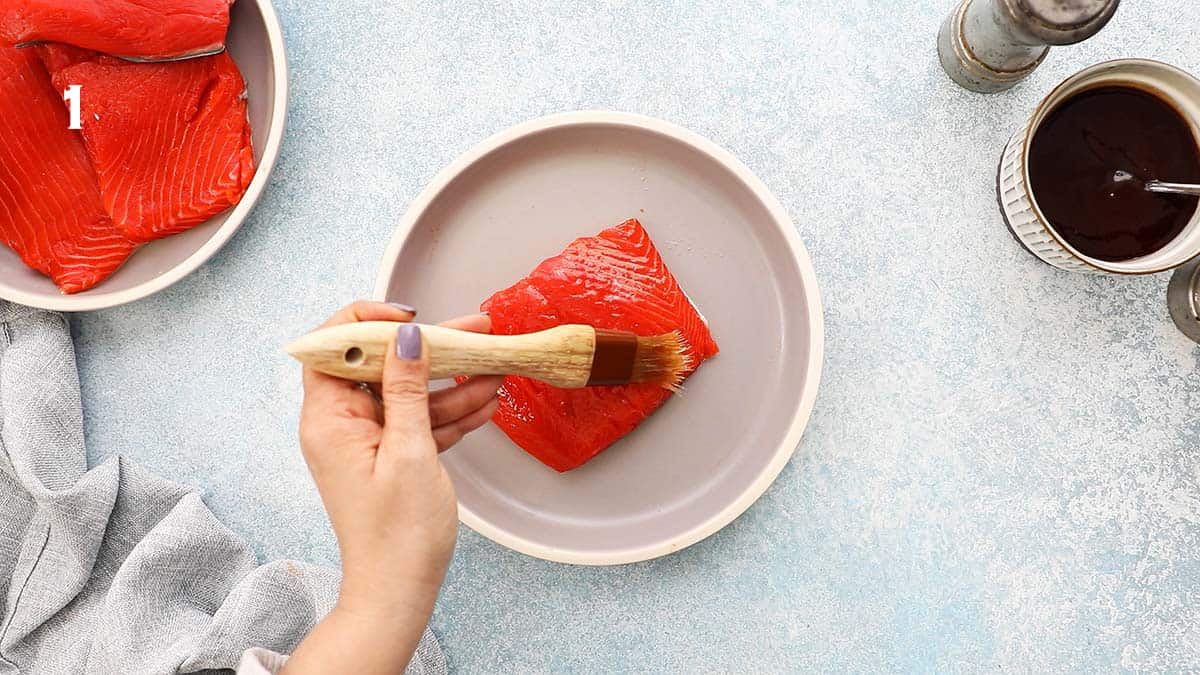 a hand brushing oil on a piece of raw salmon fillet.