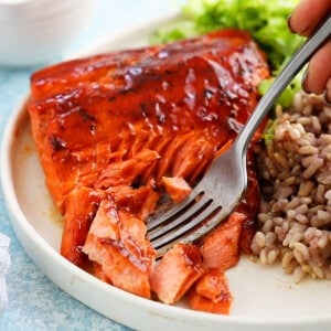 A fork taking a bite of cooked salmon from a white plate.