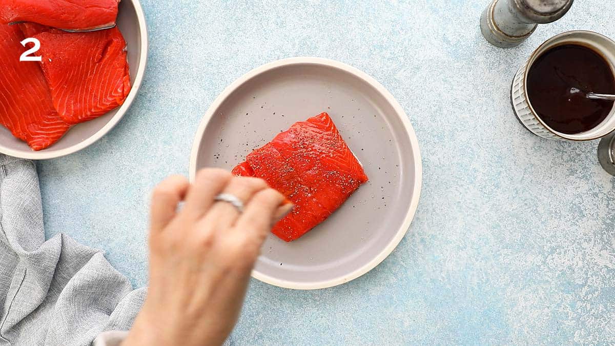 a hand sprinkling salt on a piece of raw salmon fillet.