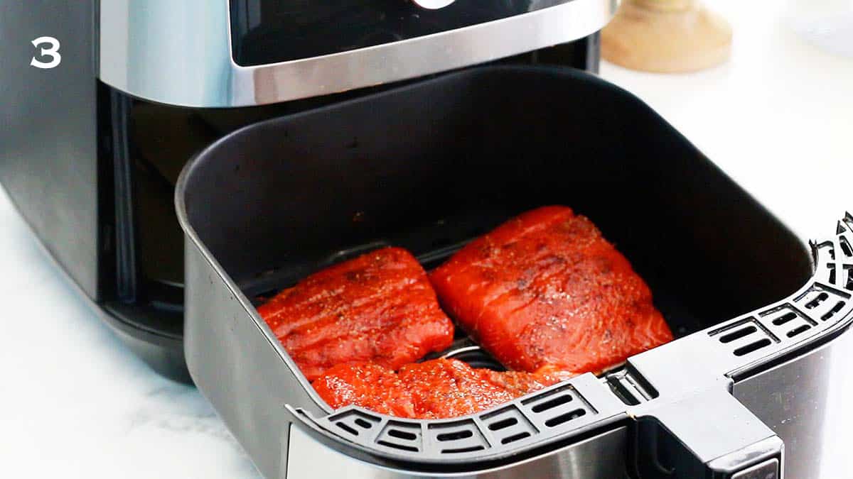 an air fryer basket with 3 raw salmon fillets.