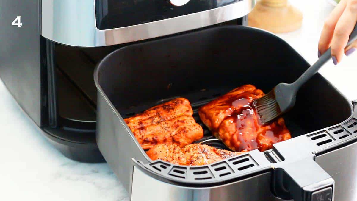 a hand brushing sauce on a cooked salmon in an open air fryer basket.