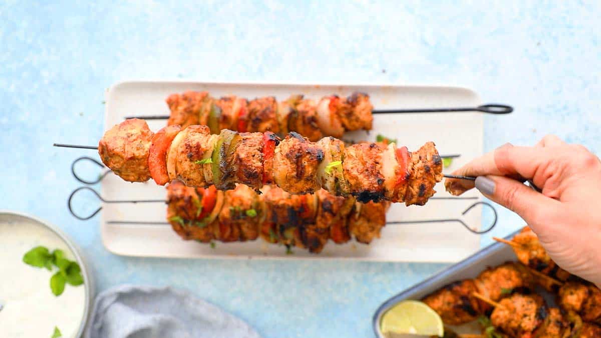 a hand holding a cooked chicken kebob skewer.