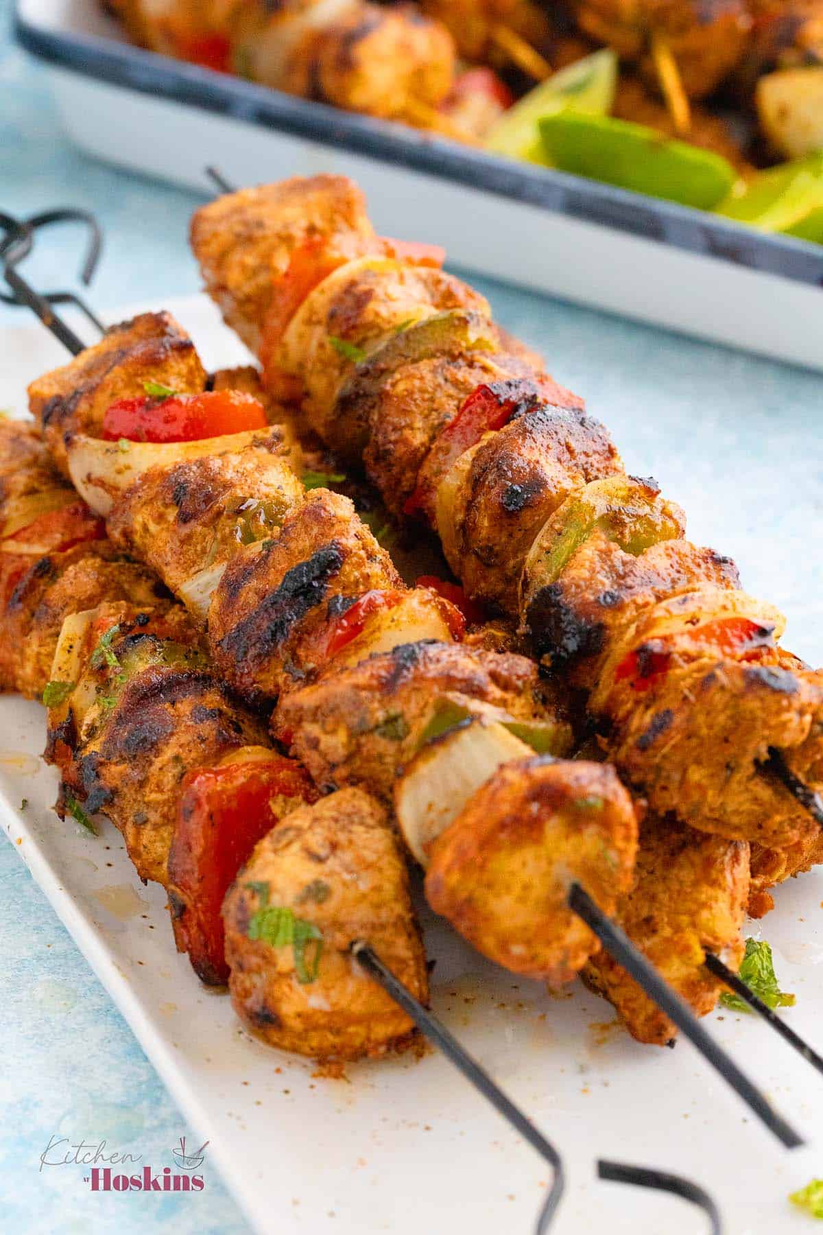 cooked chicken and veggie kebabs piled high on a white tray.