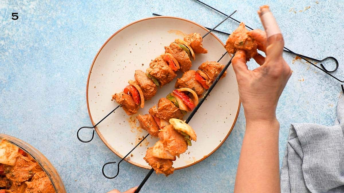 two hands threading chicken into a black skewer.