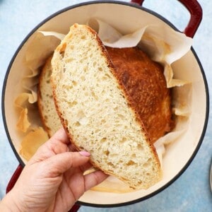 a hand holding a slice of bread above a dutch oven.