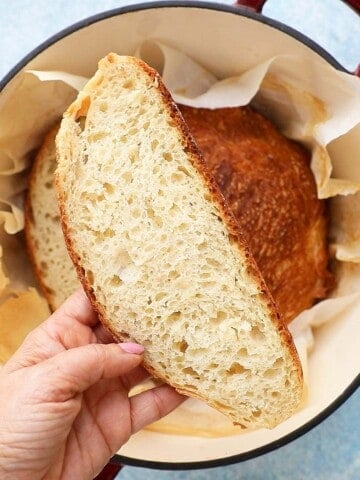 a hand holding a slice of bread above a dutch oven.