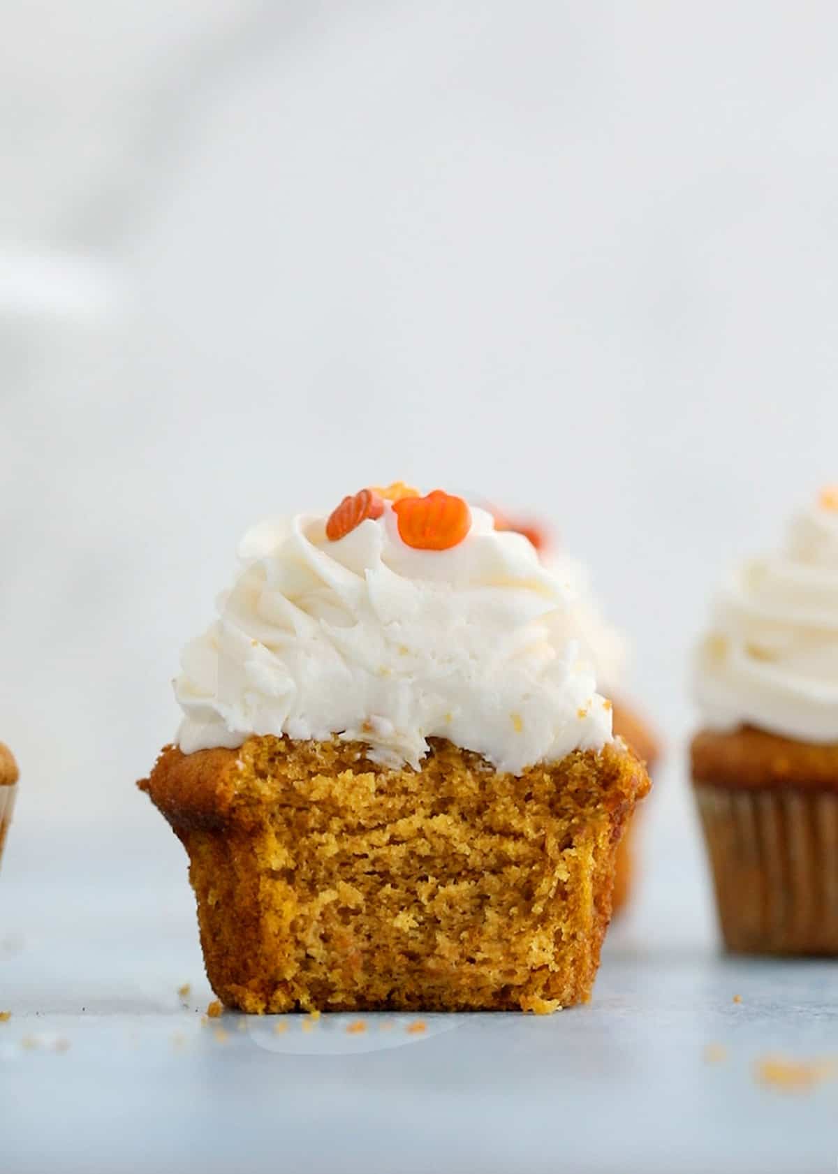 a cut pumpkin cupcake  with frosting on a blue board.