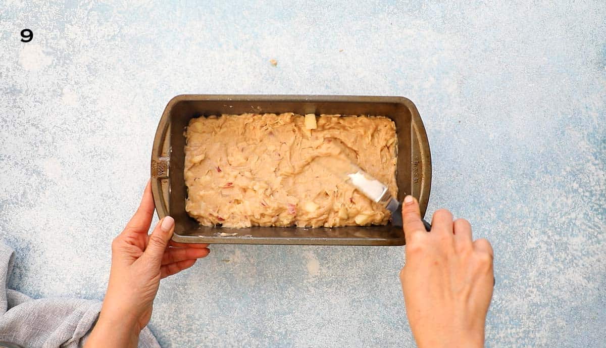 two hands spreading apple bread batter in a metal loaf pan.