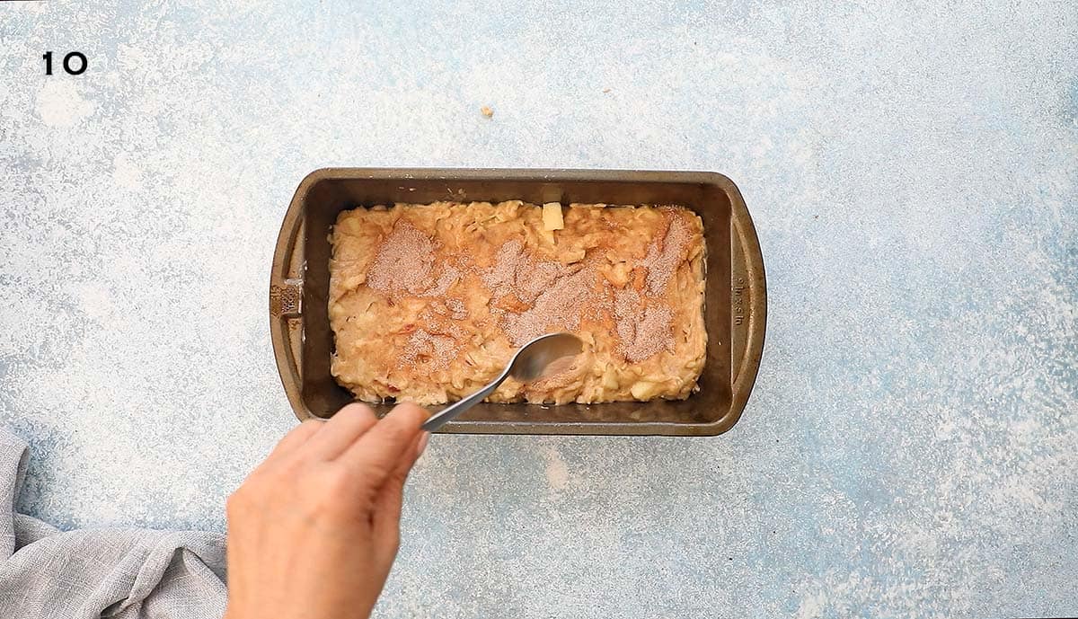 a hand sprinkling cinnamon sugar on top of batter in a metal loaf pan.
