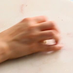 one hand rolling a bread dough on a white marble.