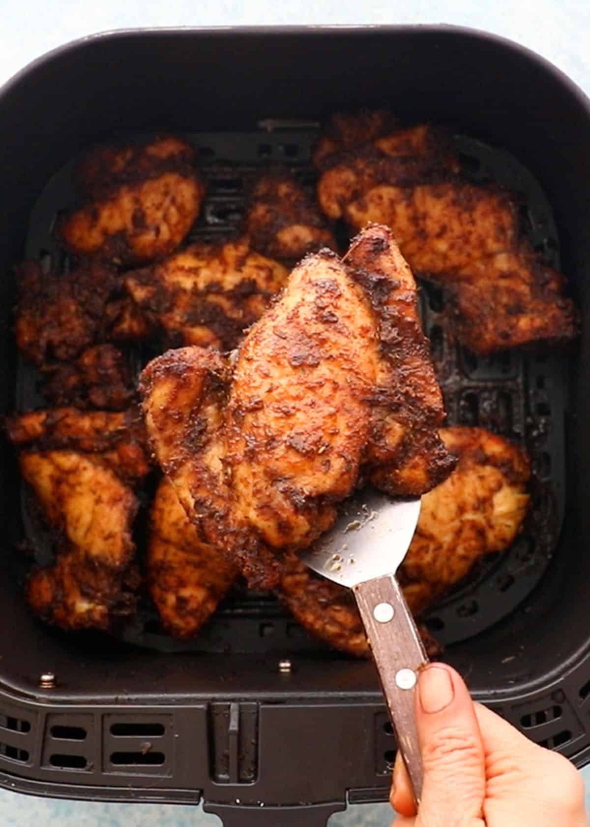 cooked brown chicken in a black air fryer basket.