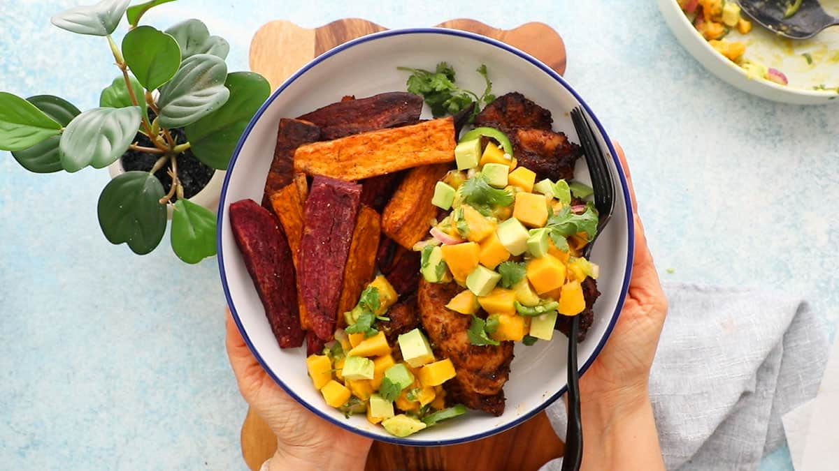 blackened chicken topped with yellow and green salsa in a white bowl.