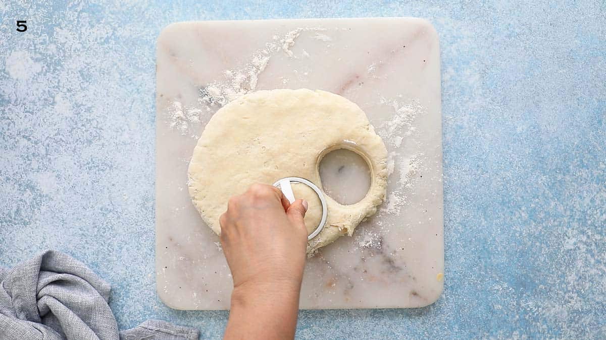 a hand cutting dough using a white handled biscuit cutter.