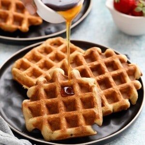 maple syrup pouring on 3 waffles on a black plate.