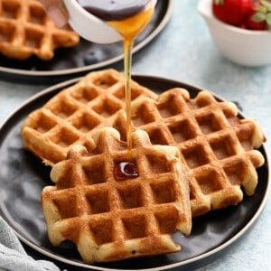 maple syrup pouring on 3 waffles on a black plate.