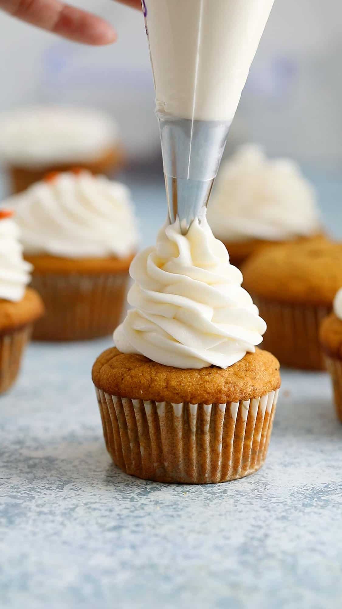 frosting being piped on a pumpkin cupcake using piping bag.