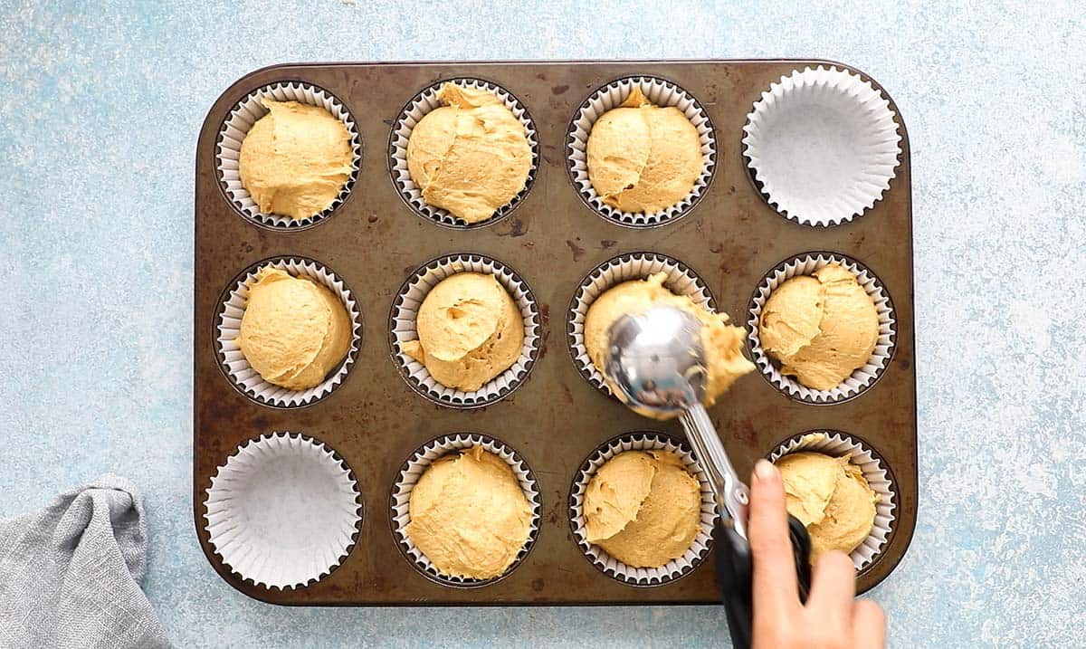 a hand filling a cupcake pan with pumpkin cupcake batter.