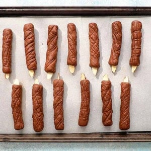 brown candle shaped cookies on a white paper lined baking sheet.