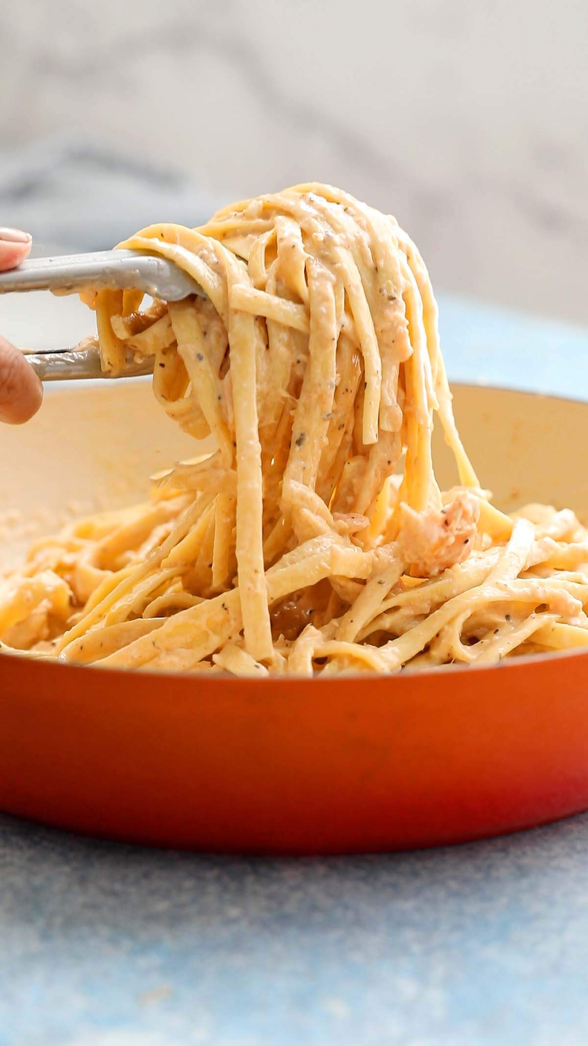 a hand serving cooked fettuccini using tongs.