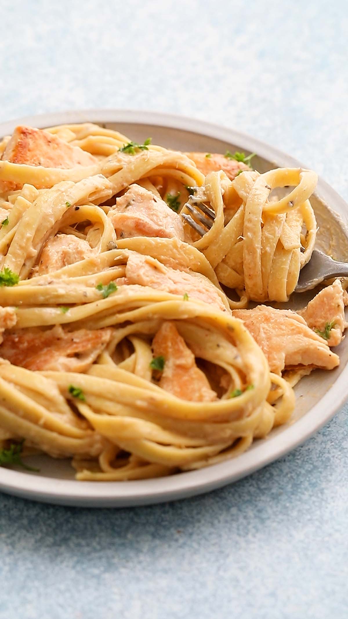 a white plate with cooked fettuccini and salmon along with a fork.