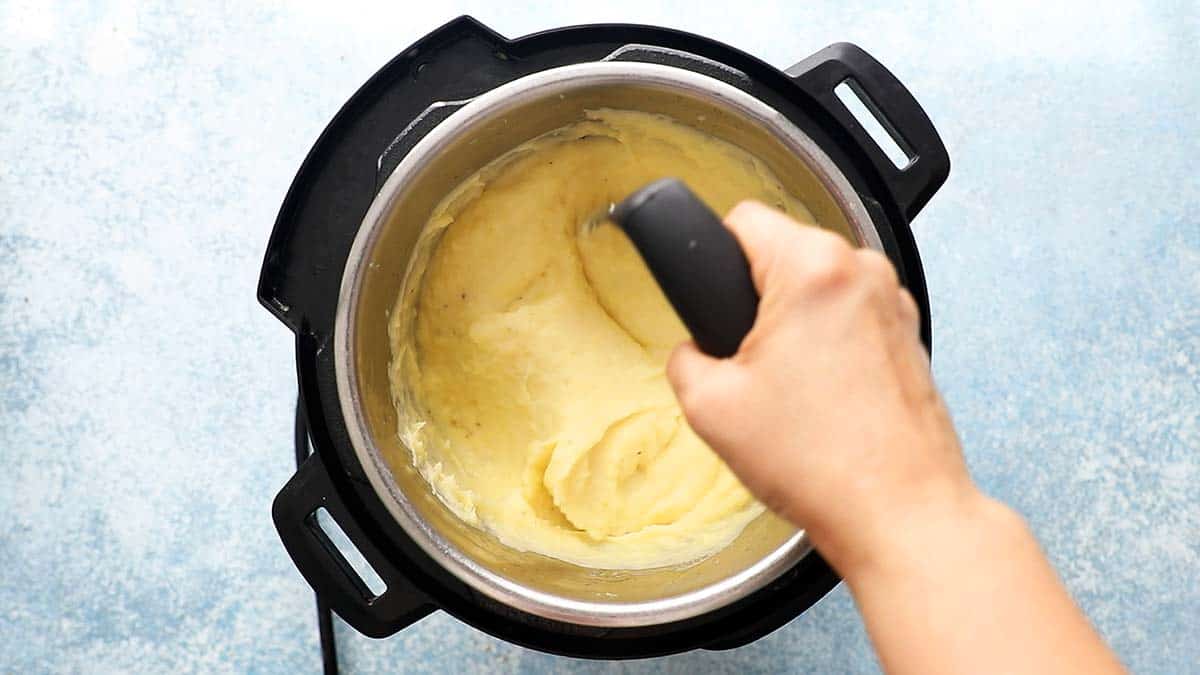 a hand mashing potatoes in an instant pot using a potato masher.