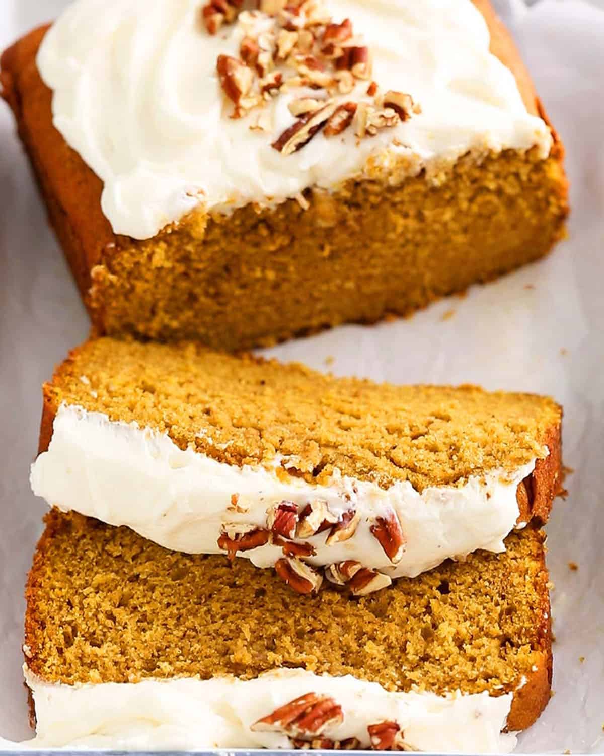 sliced orange pumpkin cake with white frosting in a white tray.