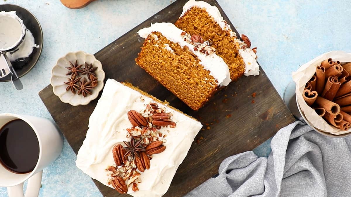 one orange pumpkin loaf cake with white frosting on a black board.