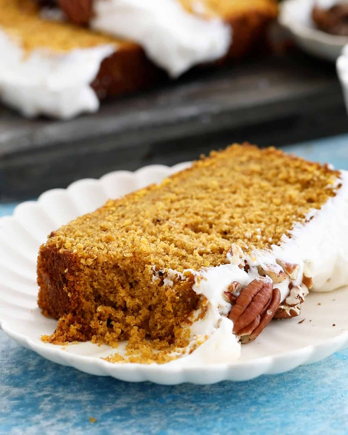 one slice of orange pumpkin cake with white frosting in a white plate.