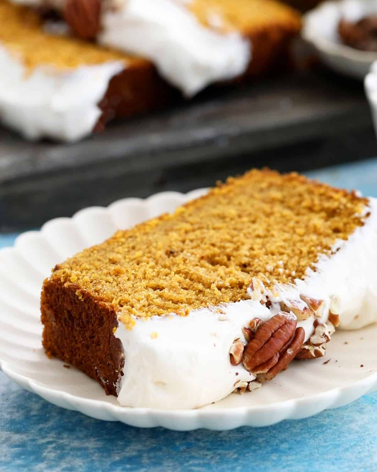 one slice of orange pumpkin cake with white frosting in a white plate.