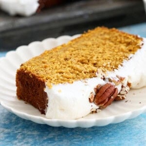 one slice of orange pumpkin cake with white frosting in a white plate.
