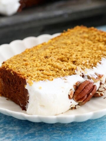 one slice of orange pumpkin cake with white frosting in a white plate.