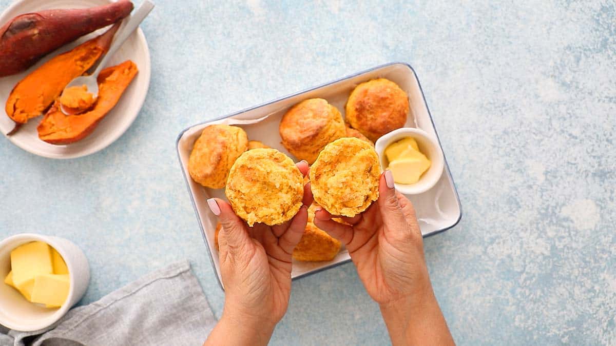 two hands holding a split open sweet potato biscuit.