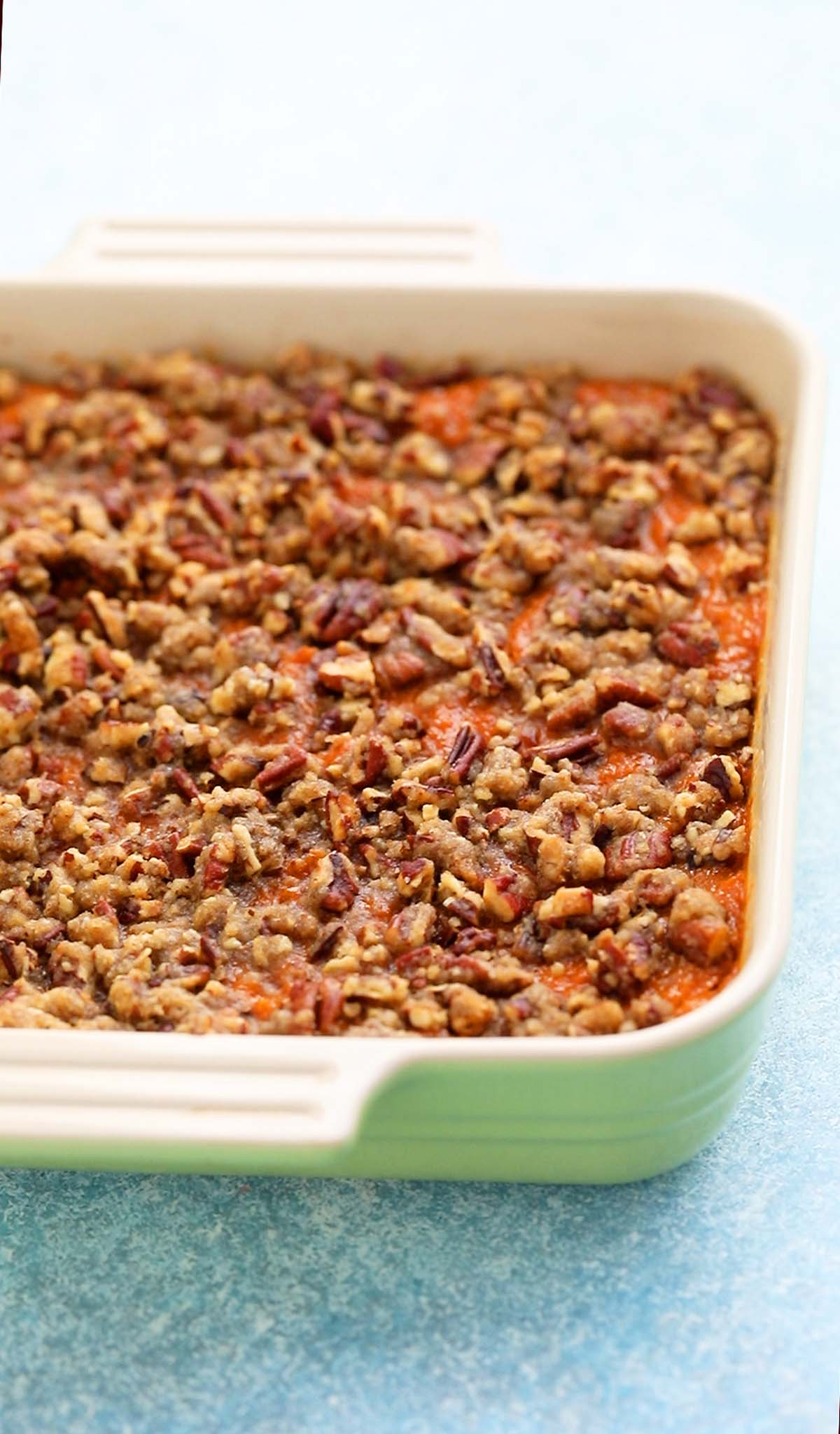 baked sweet potato souffle topped with pecans in a ceramic baking dish.