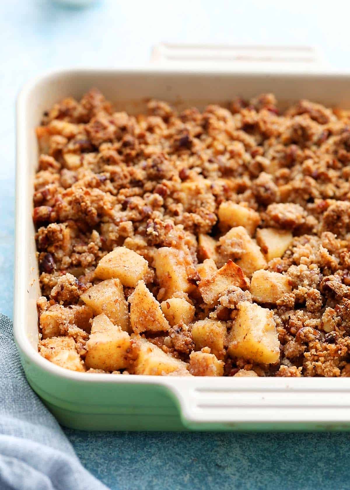 a green square baking dish with baked apple crumble.
