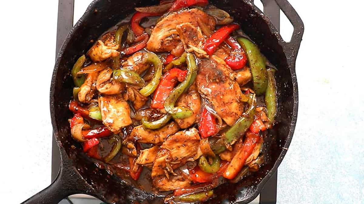 cooked black pepper chicken stir fry in a black skillet placed on a stove.