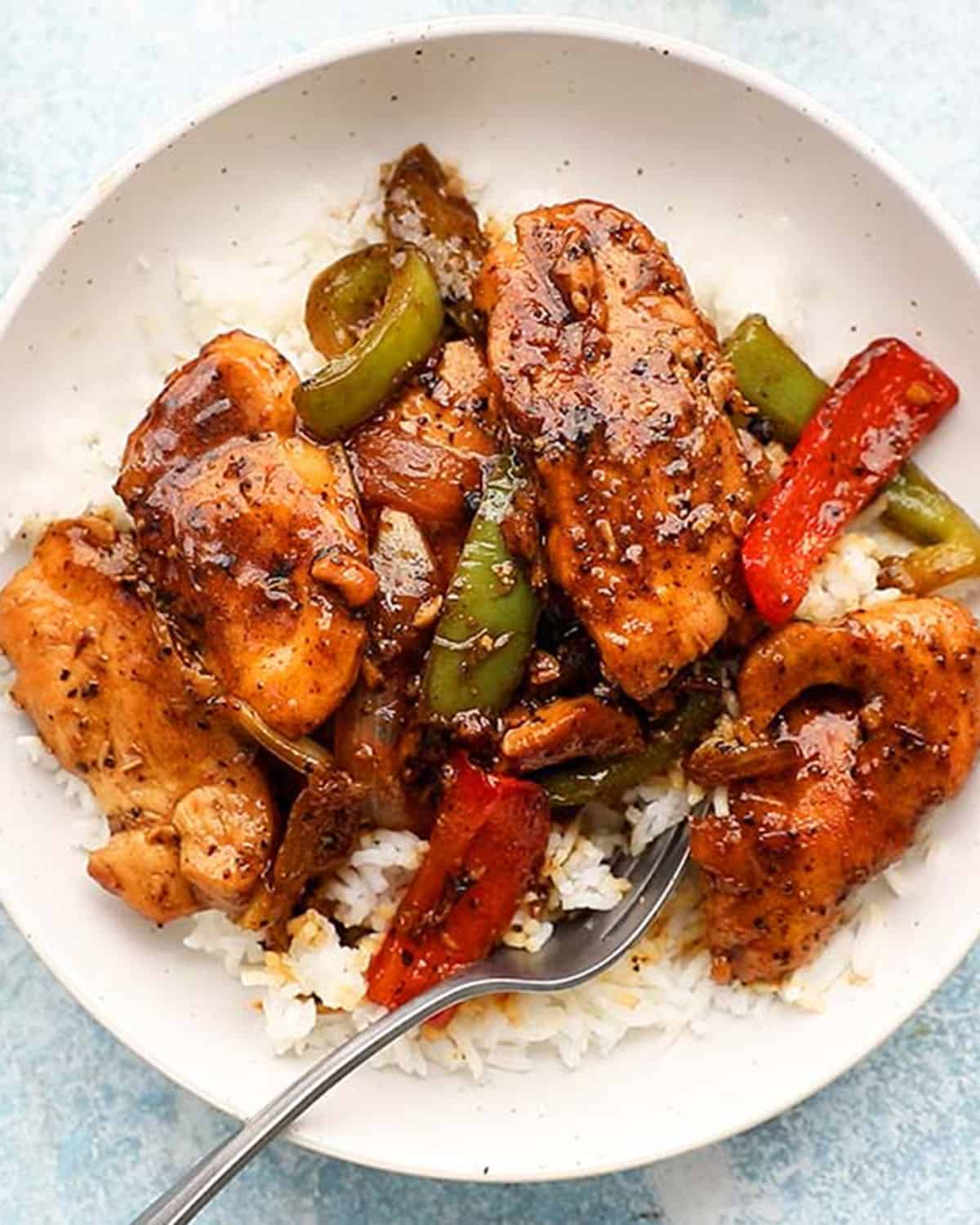 black pepper chicken stir fry with white rice in a white bowl and a metal fork.